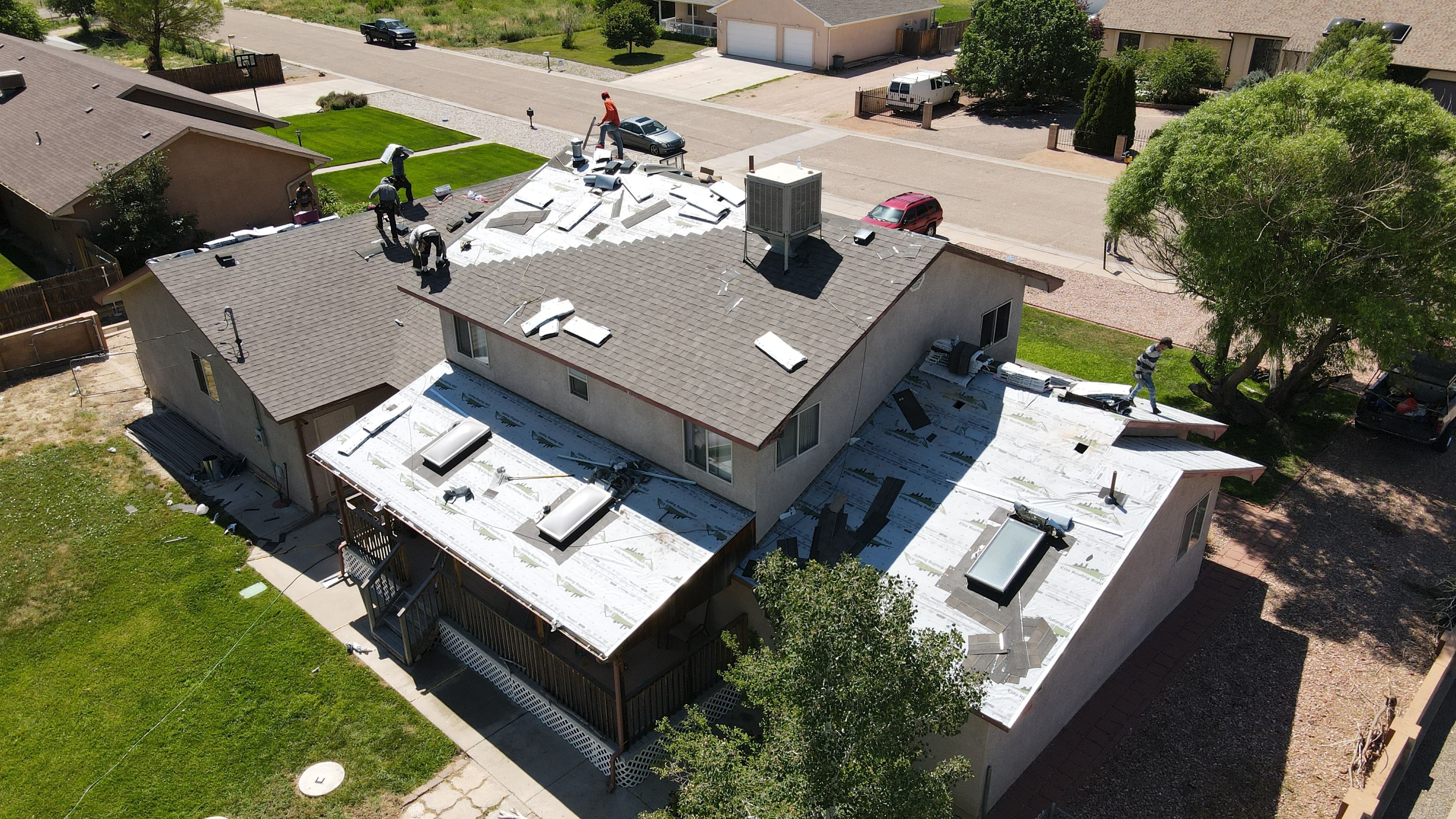 Roof replacement in progress on residential home with workers and materials visible.