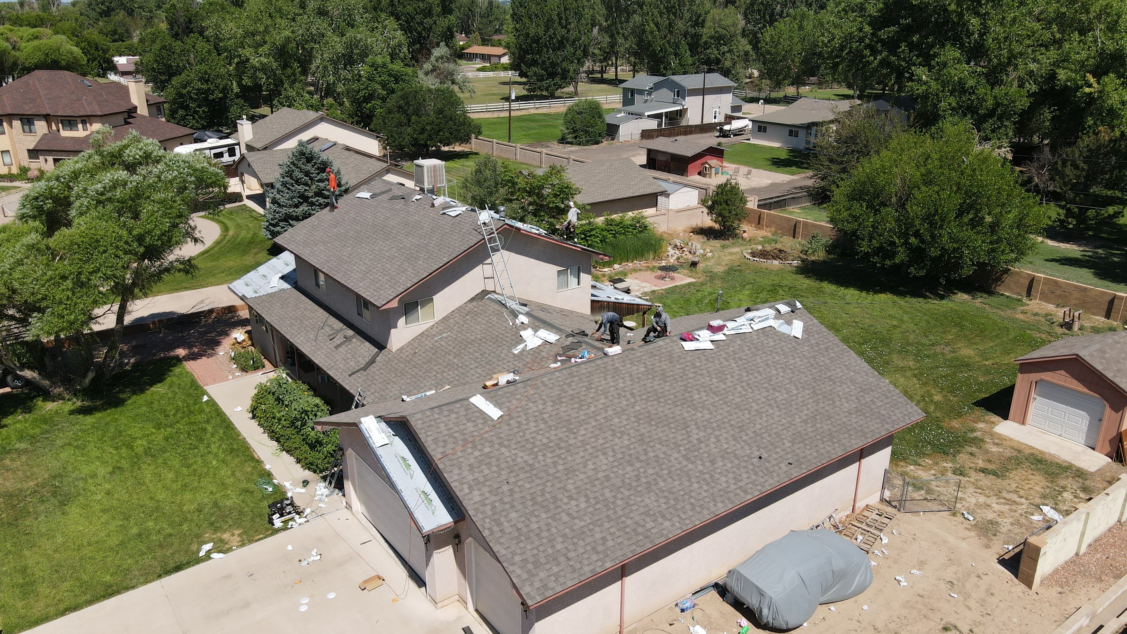 Aerial view of a home undergoing roof installation with crews on the roof and surrounding landscape.