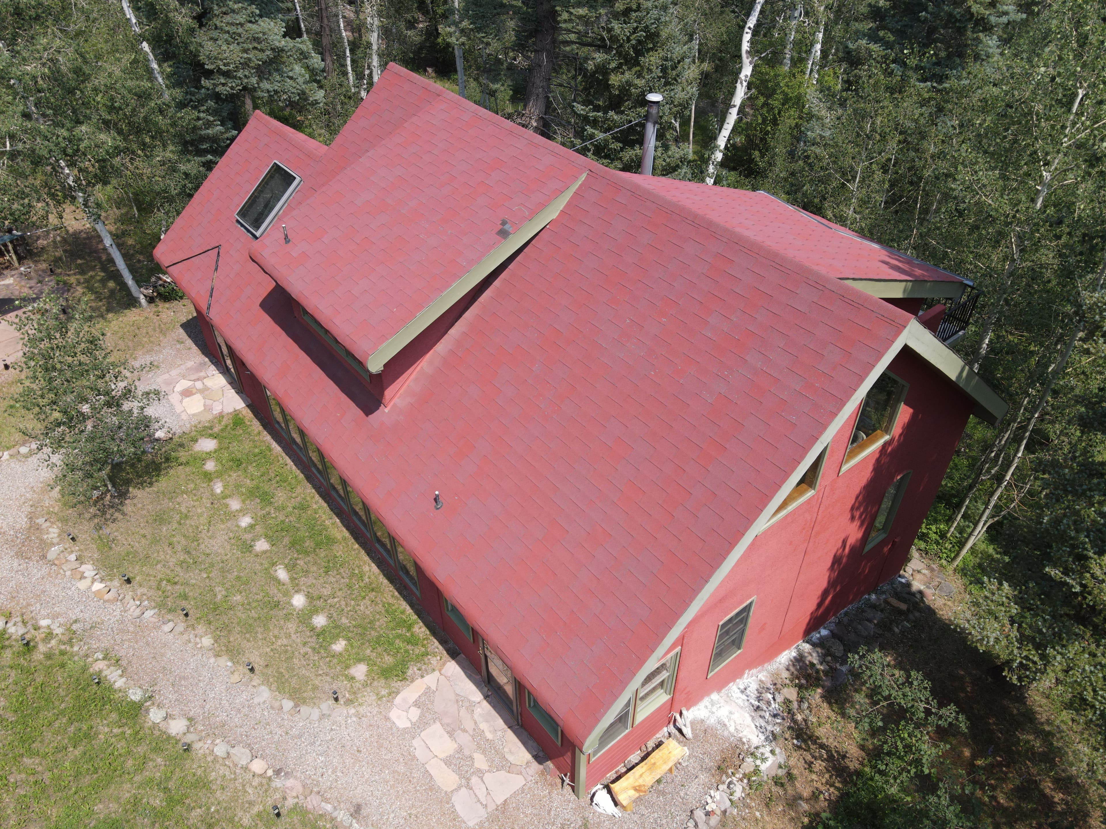 Aerial view of a red house with a sloped roof surrounded by greenery and a stone pathway.