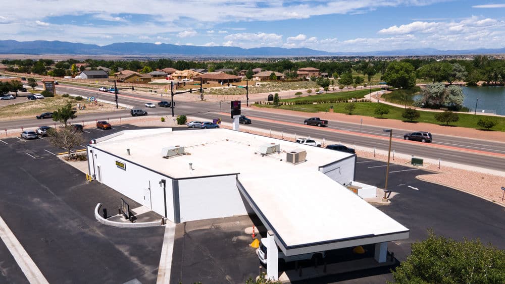 Aerial view of a commercial building near a highway, surrounded by residential area and park.