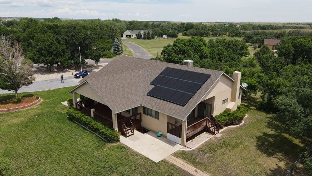 Aerial view of a house with solar panels, surrounded by green trees and open space.